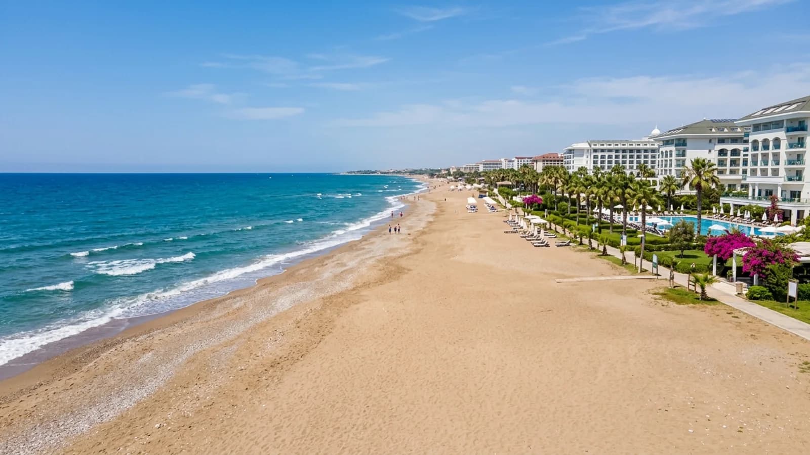 Ein langer goldener Sandstrand in Kızılağaç mit weißen Hotelanlagen, Palmengärten und tiefblauem Meer.