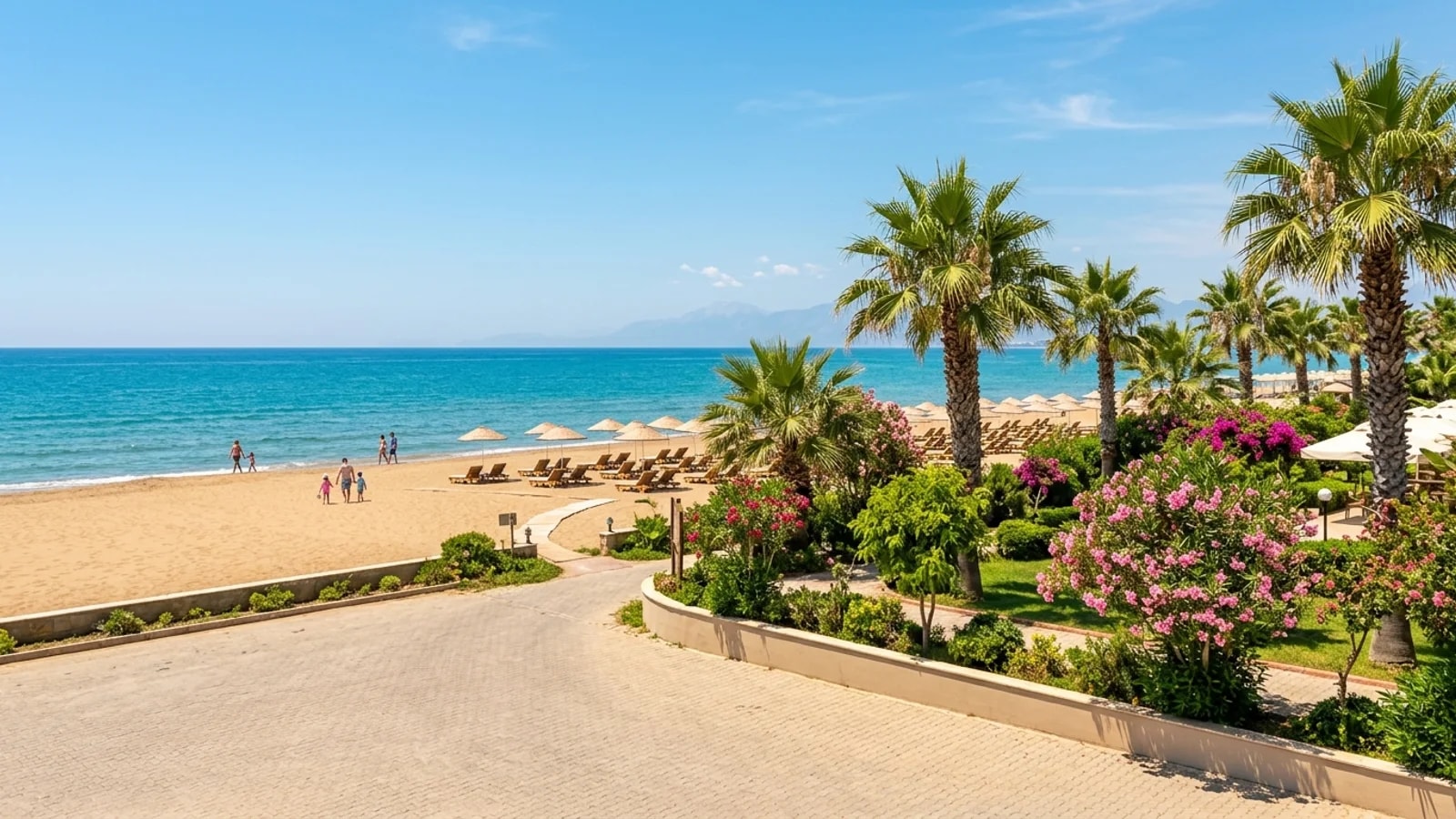 Ein breiter Sandstrand mit Liegestühlen an ruhigem, türkisblauem Wasser vor den fernen Ausläufern des Taurusgebirges.