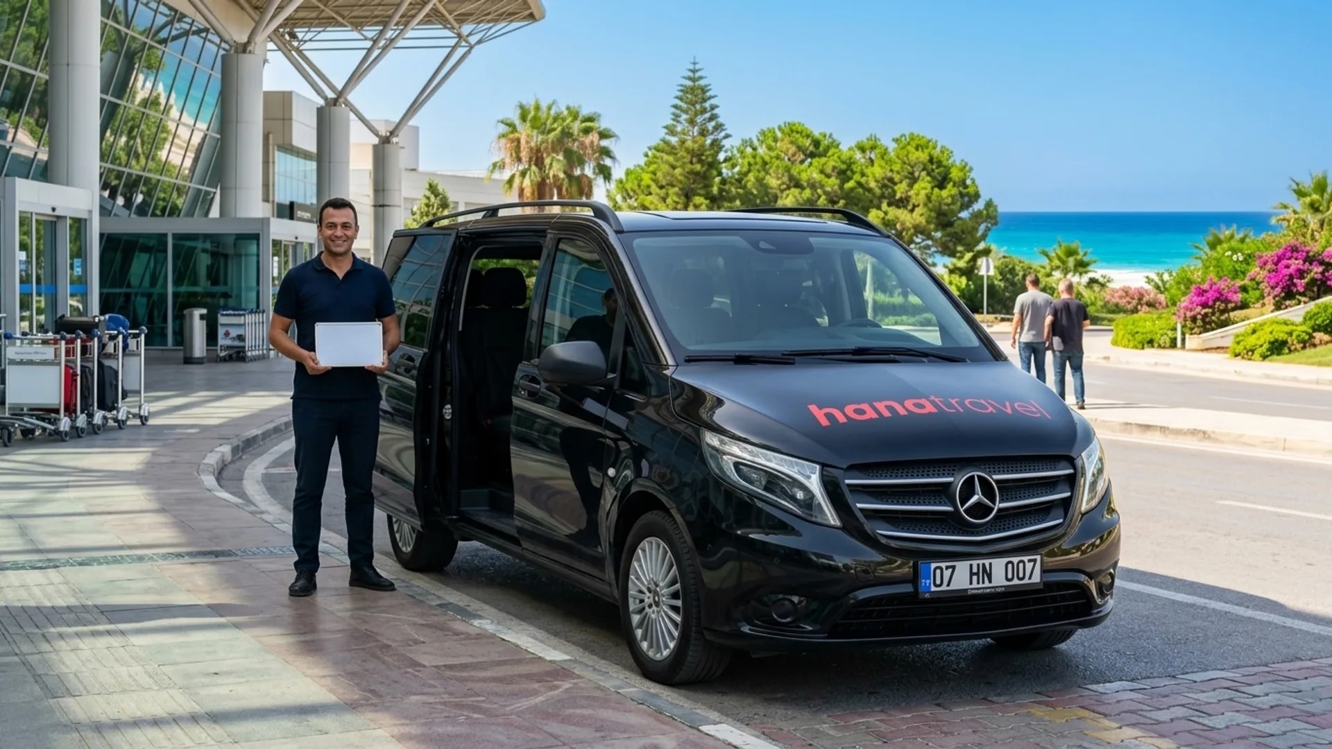 Look for your name outside arrivals Smiling Hana Travel driver with a name board next to the black Vito outside the arrivals hall at Antalya Airport — Side airport transfer
